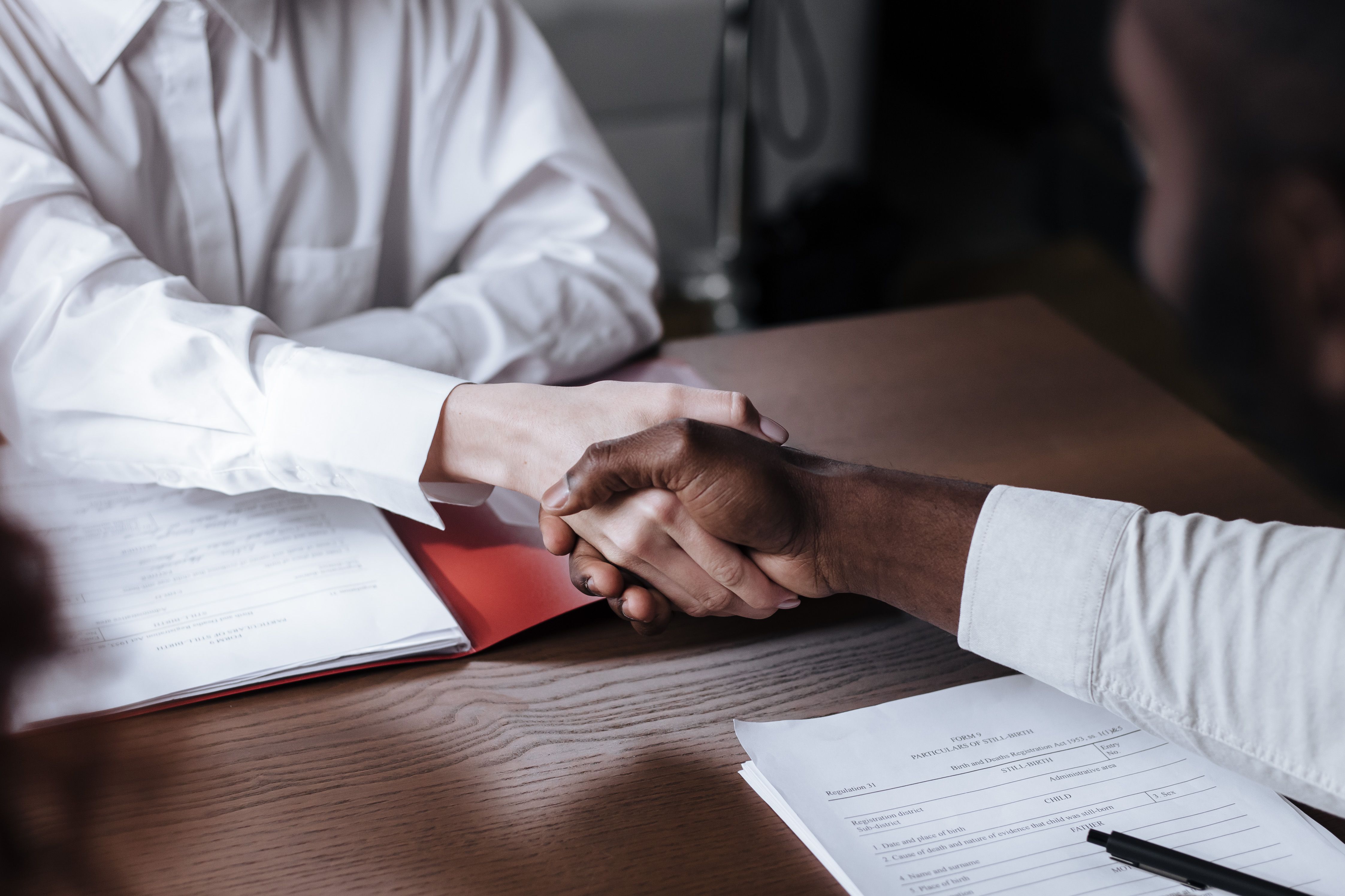 Diverse business handshake over documents symbolizing due diligence and financial partnership checks