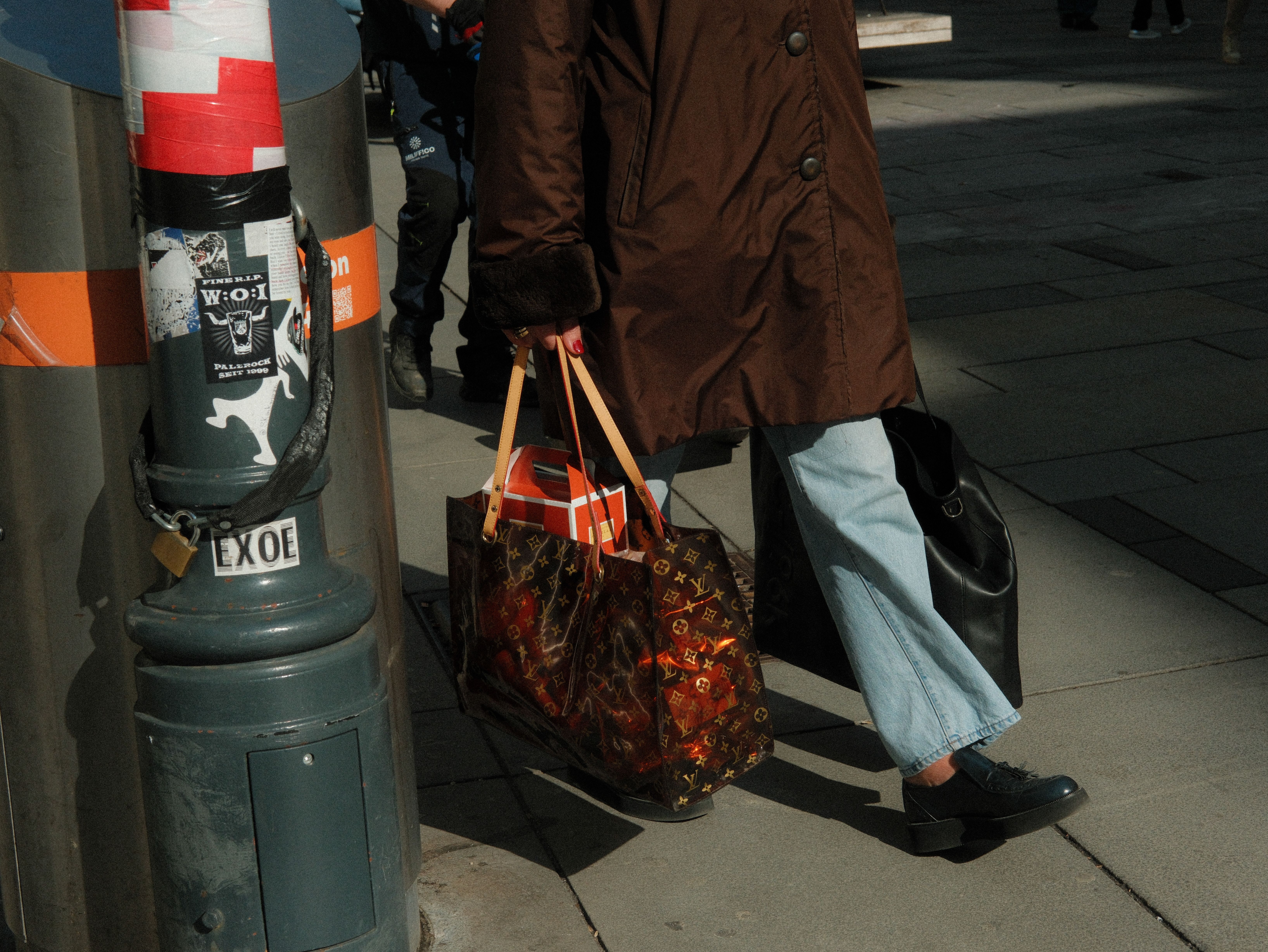 Person in stylish attire walking a city street carrying luxury brand shopping bags
