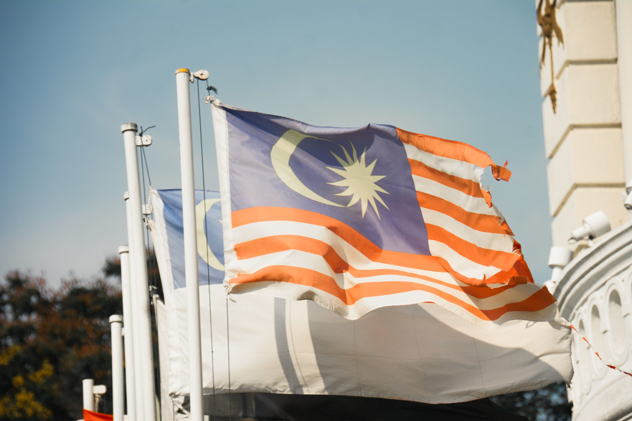 Malaysian flag waving against a clear blue sky, symbolizing national politics and Anwar's coalition