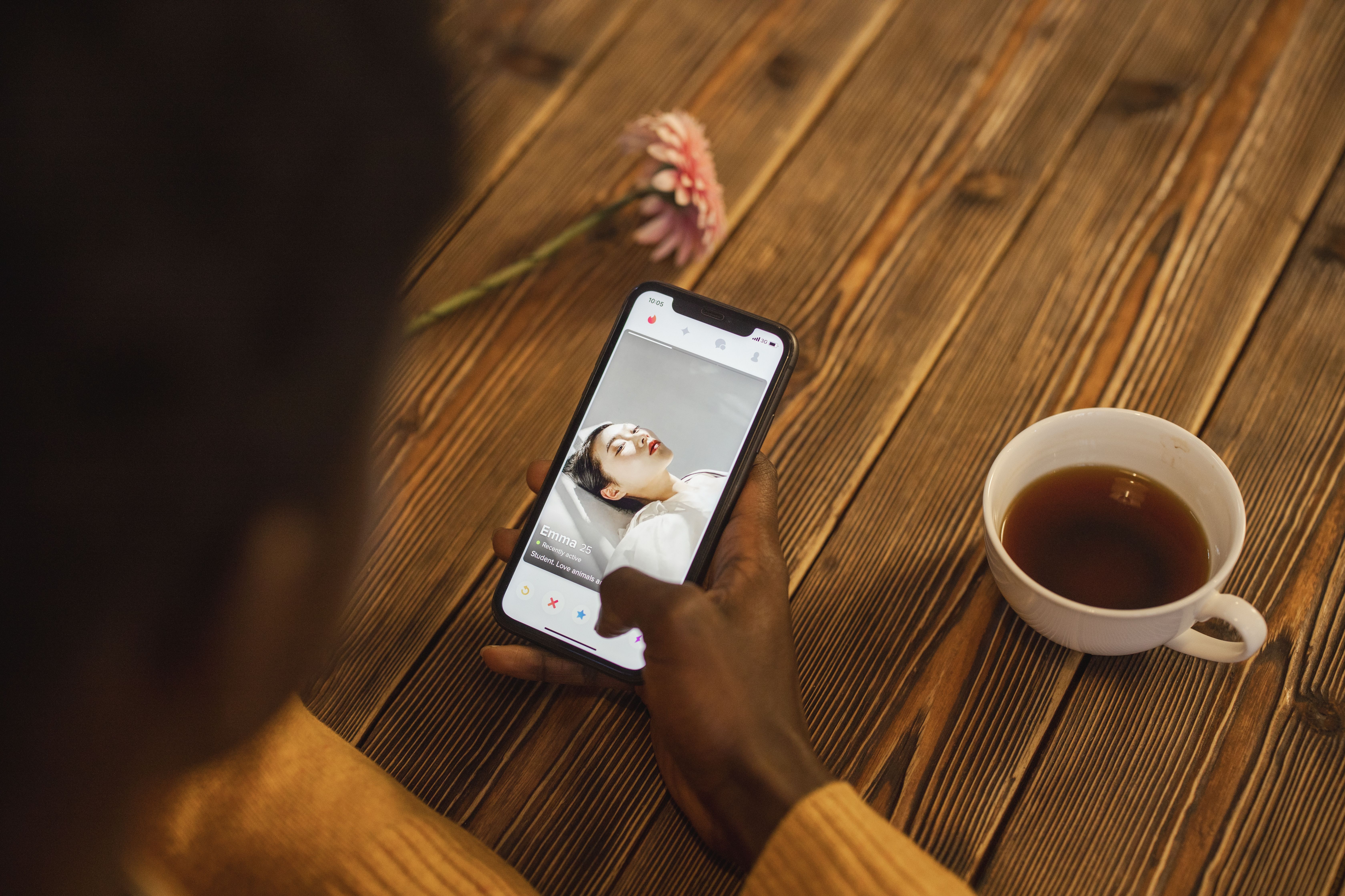 Person exploring a dating app on a smartphone beside a cup of tea.