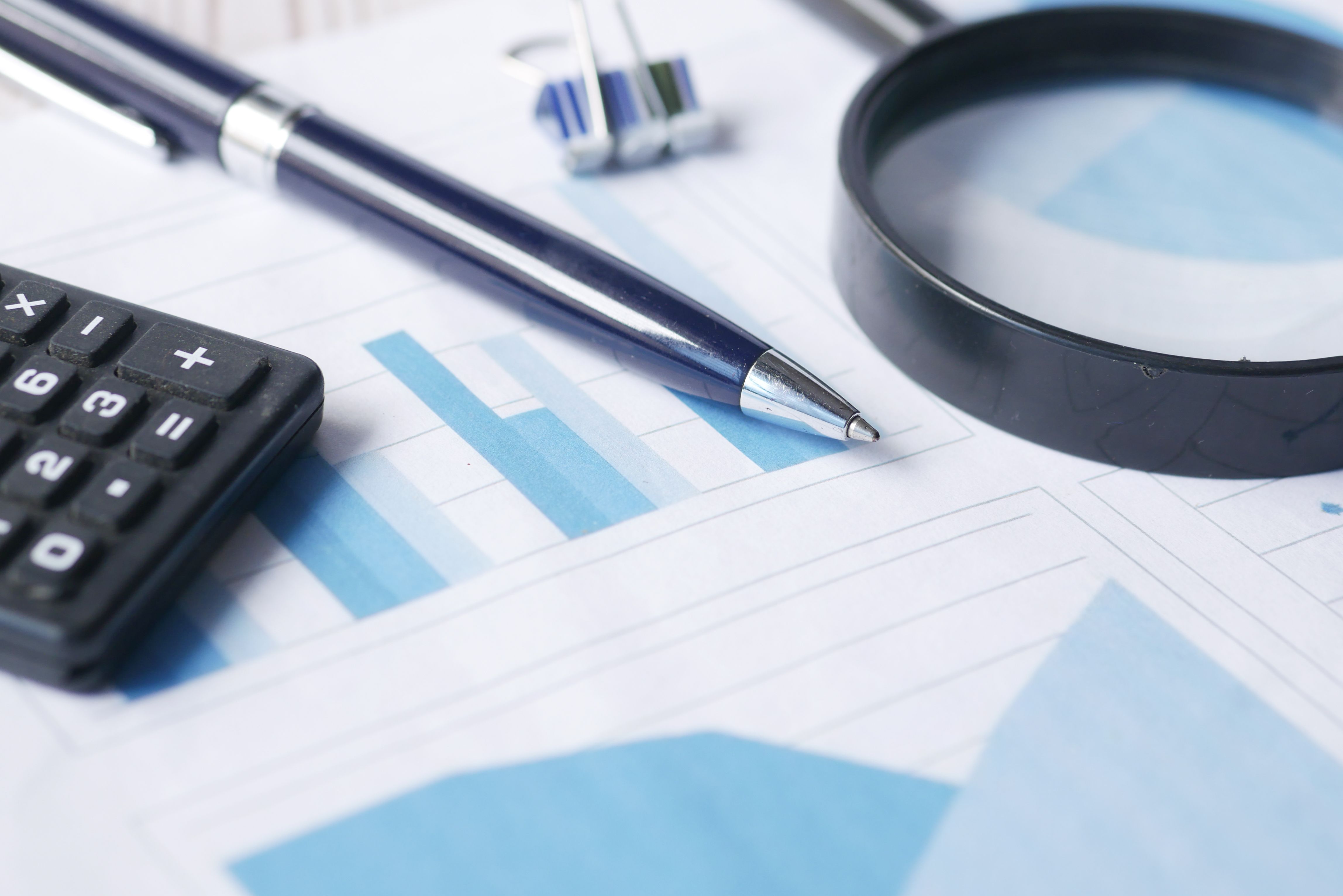 Calculator, pen, and magnifying glass used to review financial documents