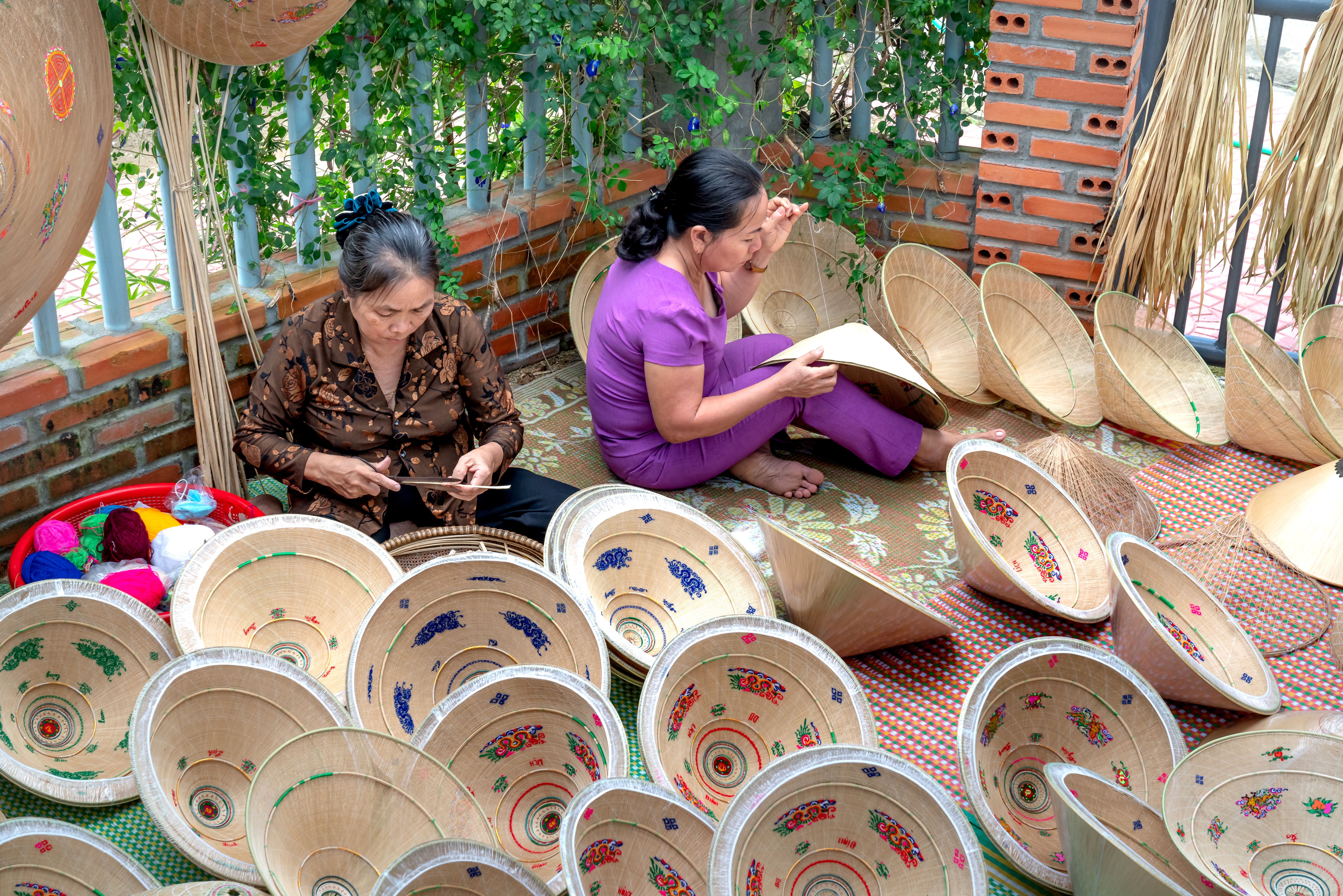 Two artisans crafting traditional Vietnamese conical hats with colorful decorations outdoors